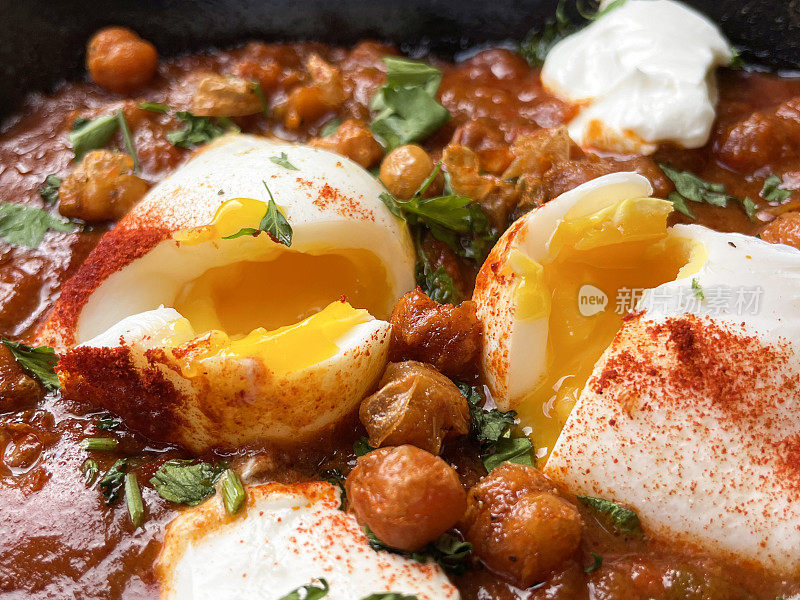 一锅地中海健康早餐的全画幅图片:shakshouka / shakshuka / chakchouka，鹰嘴豆，鸡蛋在番茄，辣椒，洋葱，橄榄油和大蒜的酱汁中水煮，顶部有香菜，高架视图，重点在前景